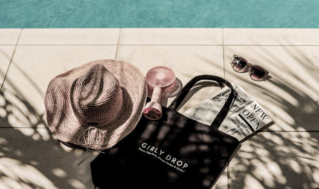 プールサイドに置かれた黒いバッグと麦わら帽子と携帯ファンとサングラス