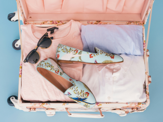 洋服・サングラス・花柄のパンプスが入っているピンクのスーツケース
